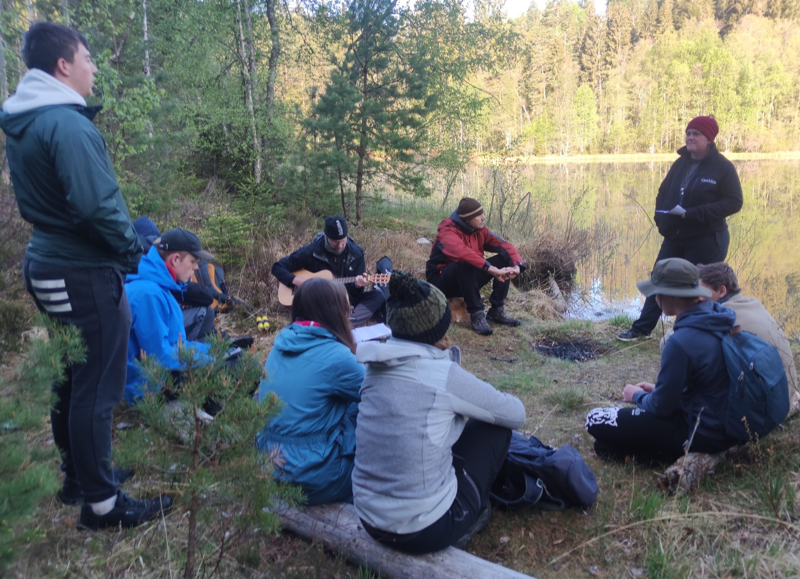 Ett gäng barn står med händerna uppsträckta och tittar mot solnedgången. De ser ut som svarta silhuetter mot den blå och gula himlen.